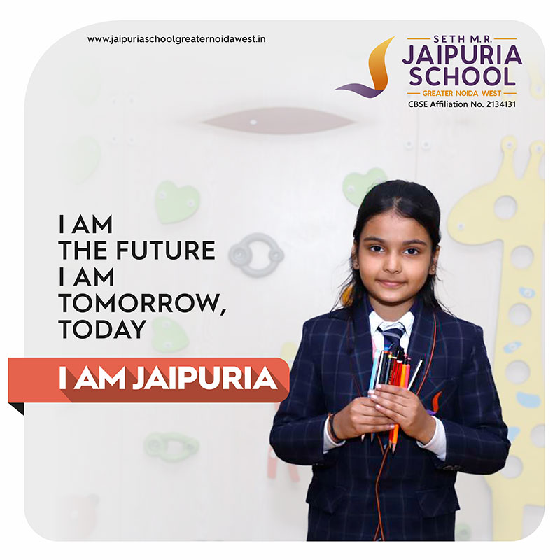 Girl in a navy plaid school uniform holding colored pencils, with the slogan 'I AM THE FUTURE I AM TOMORROW, TODAY' and the 'I AM JAIPURIA' logo in the corner.